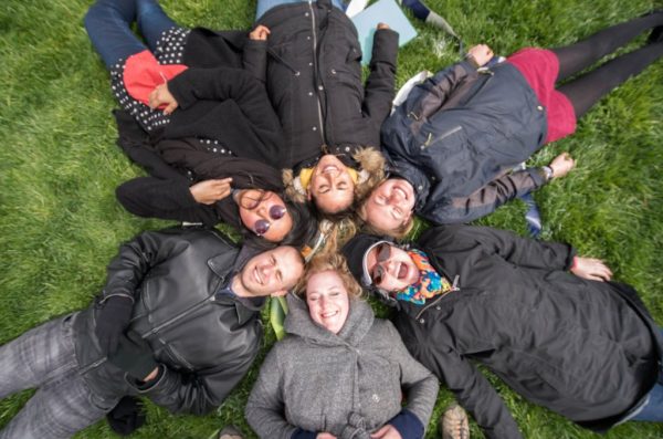 Group of people laying together in lawn with their heads close together.